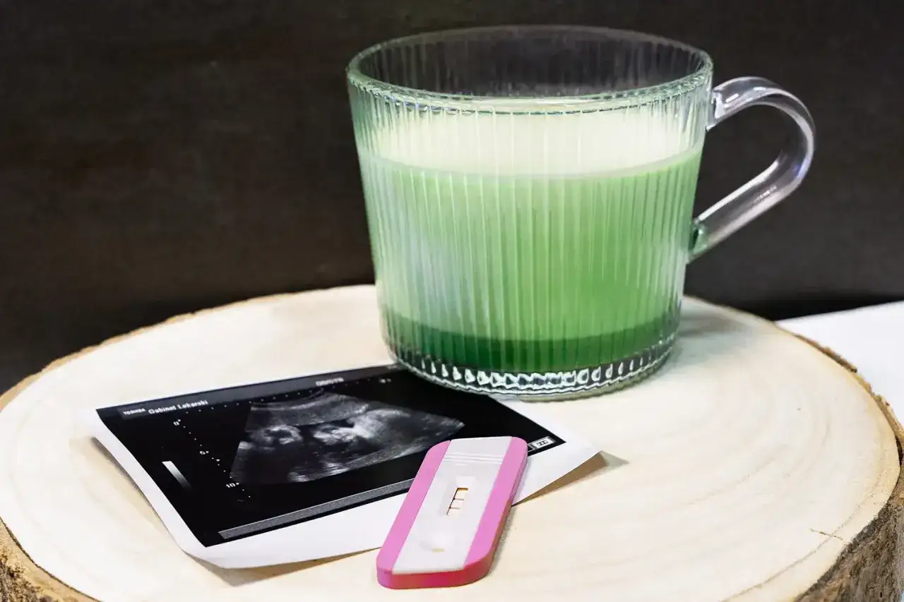 Kubek zielonego matcha latte obok pozytywnego testu ciążowego i USG. Czas na zdrowe napoje w ciąży.
