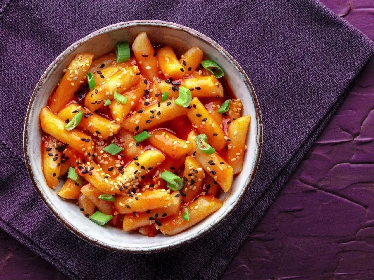 Miseczka pełna pikantnych klusek ryżowych w sosie gochujang, posypanych sezamem i szczypiorkiem.