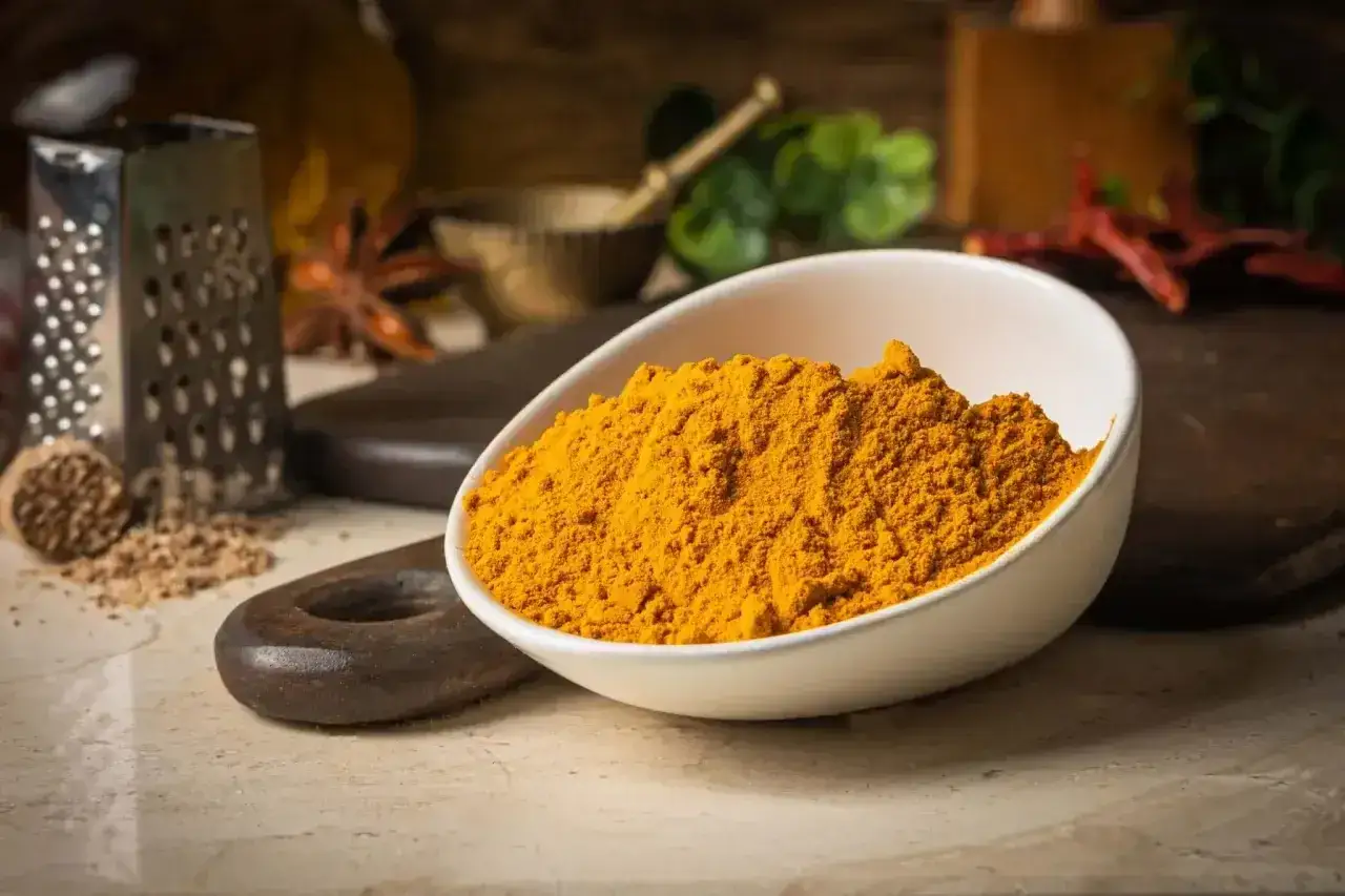 Jasna, żółta kurkuma w miseczce, gotowa do przygotowania aromatycznego curry. Obok przyprawy, tarka i inne składniki.