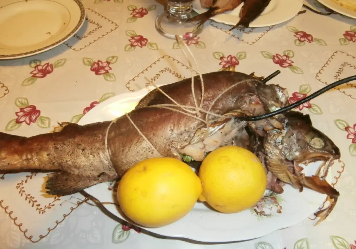 Pstrąg wędzony, związany sznurkiem, leży na talerzu z dwoma cytrynami. Idealny na rodzinny obiad.