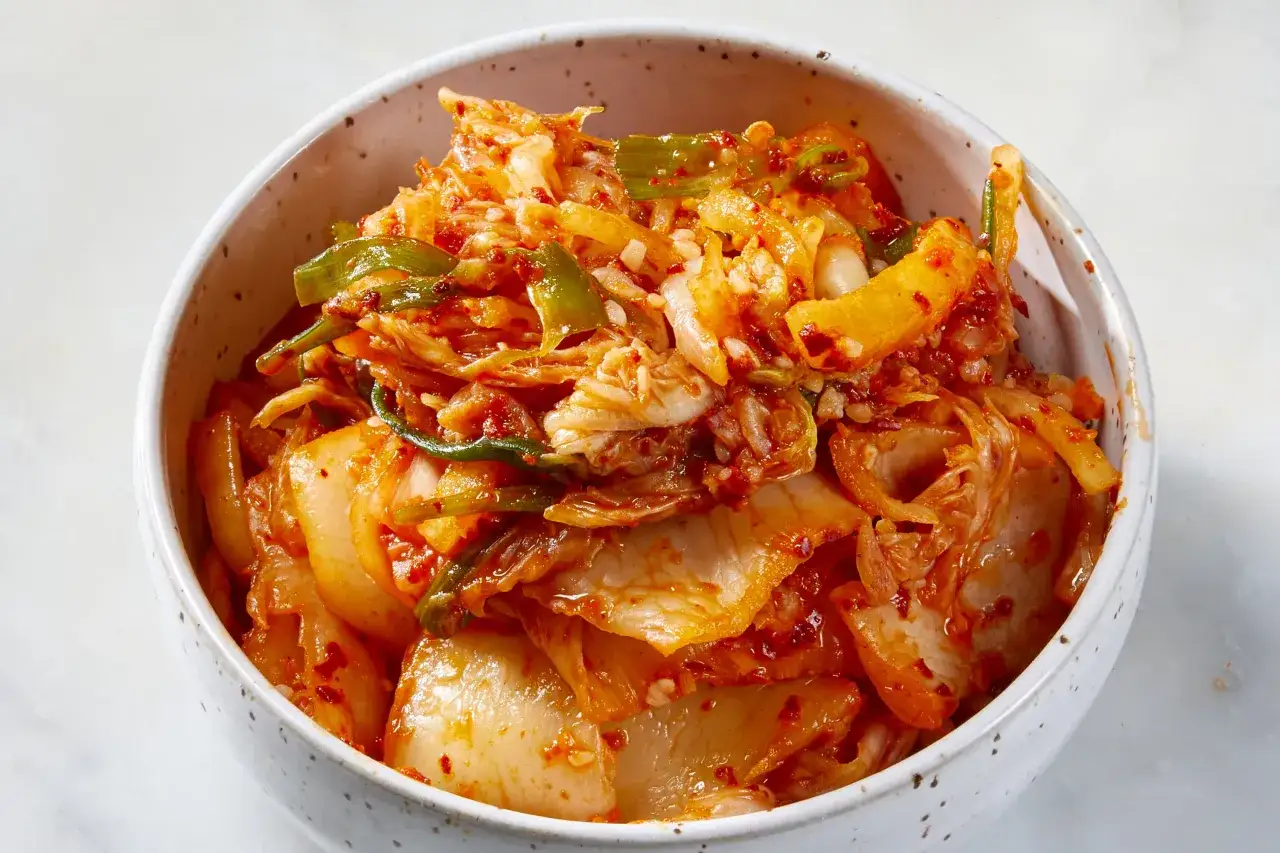 Miseczka pełna pikantnych przypraw do kimchi, z widocznymi kawałkami kapusty i zielonej cebulki, gotowa do fermentacji.