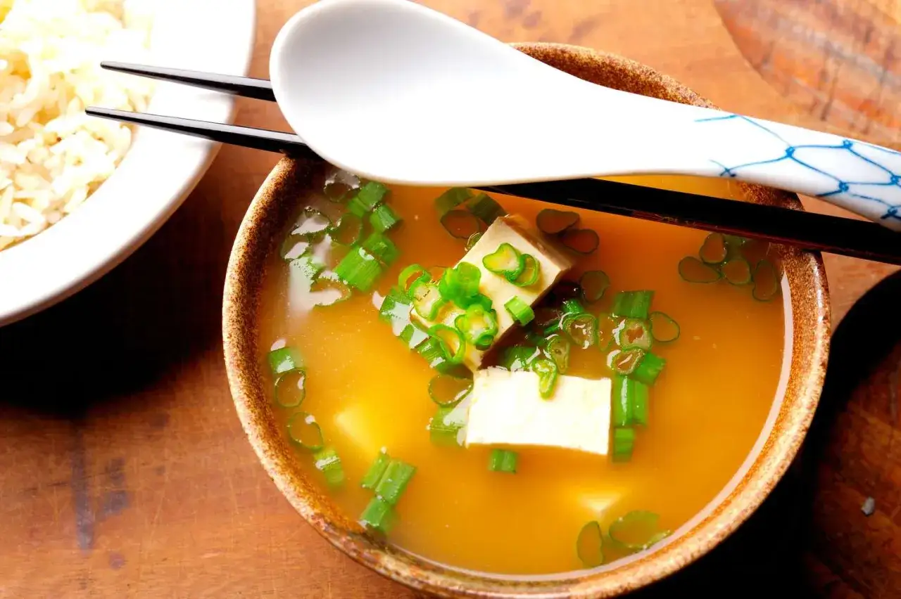 Aksamitny bulion miso z kostkami tofu i szczypiorkiem, obok miseczka ryżu.