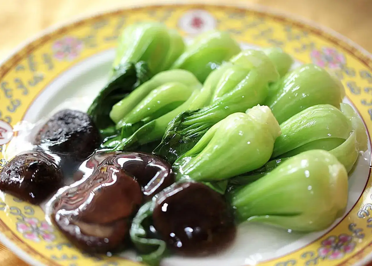Bok choy z aromatycznymi, ciemnymi chińskimi grzybami w sosie na żółtym talerzu.