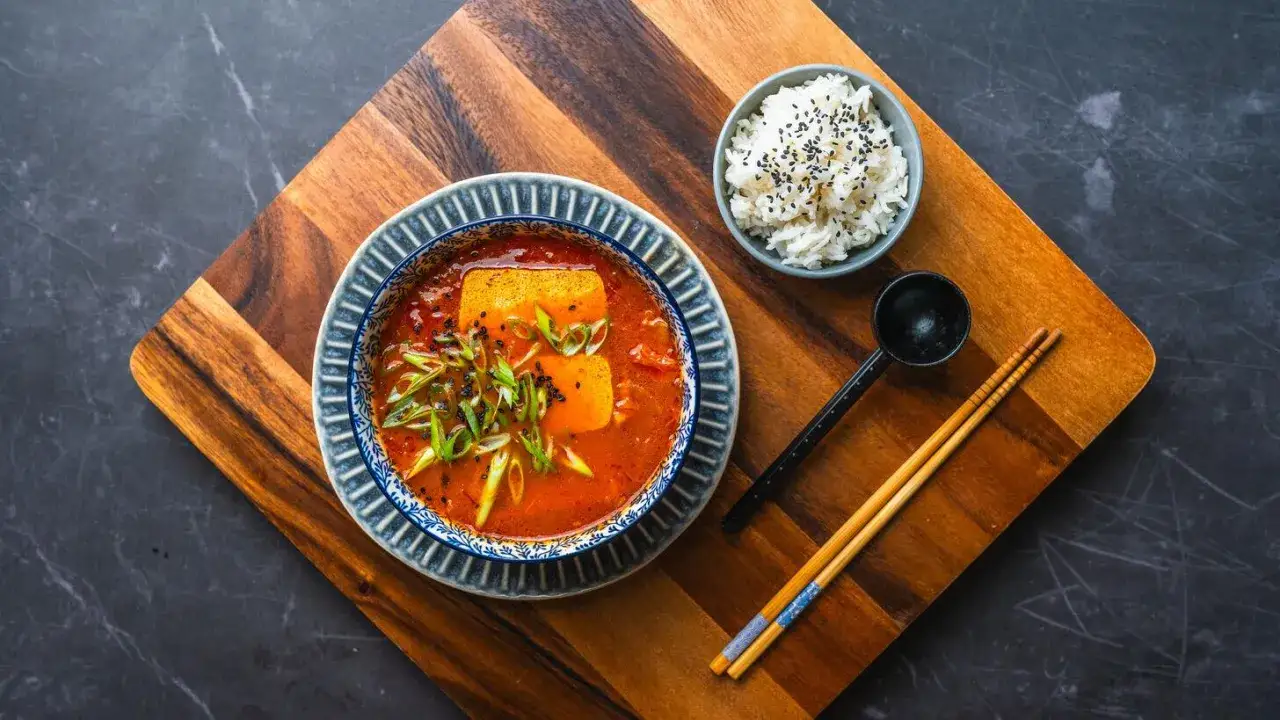 Aromaticzna zupa kimchi z kurczakiem, podana z ryżem i pałeczkami.