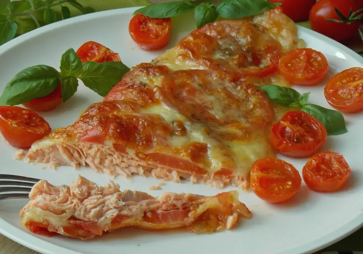 Pyszny, zapieczony filet z pstrąga z pomidorkami koktajlowymi i roztopionym serem, ozdobiony listkami bazylii.