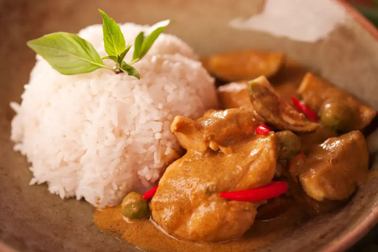 Pyszne tajskie curry z kurczakiem i ryżem, ozdobione świeżą bazylią i papryczką chili.