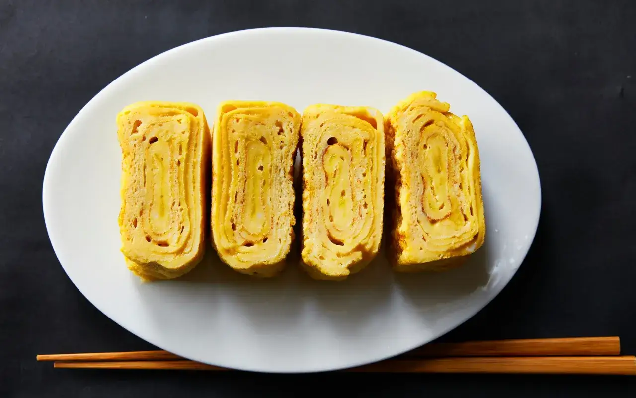 Cztery kawałki tamago, czyli japońskiego omletu, ułożone na białym talerzu. Zastanawiasz się tamago co to? To pyszna przekąska!