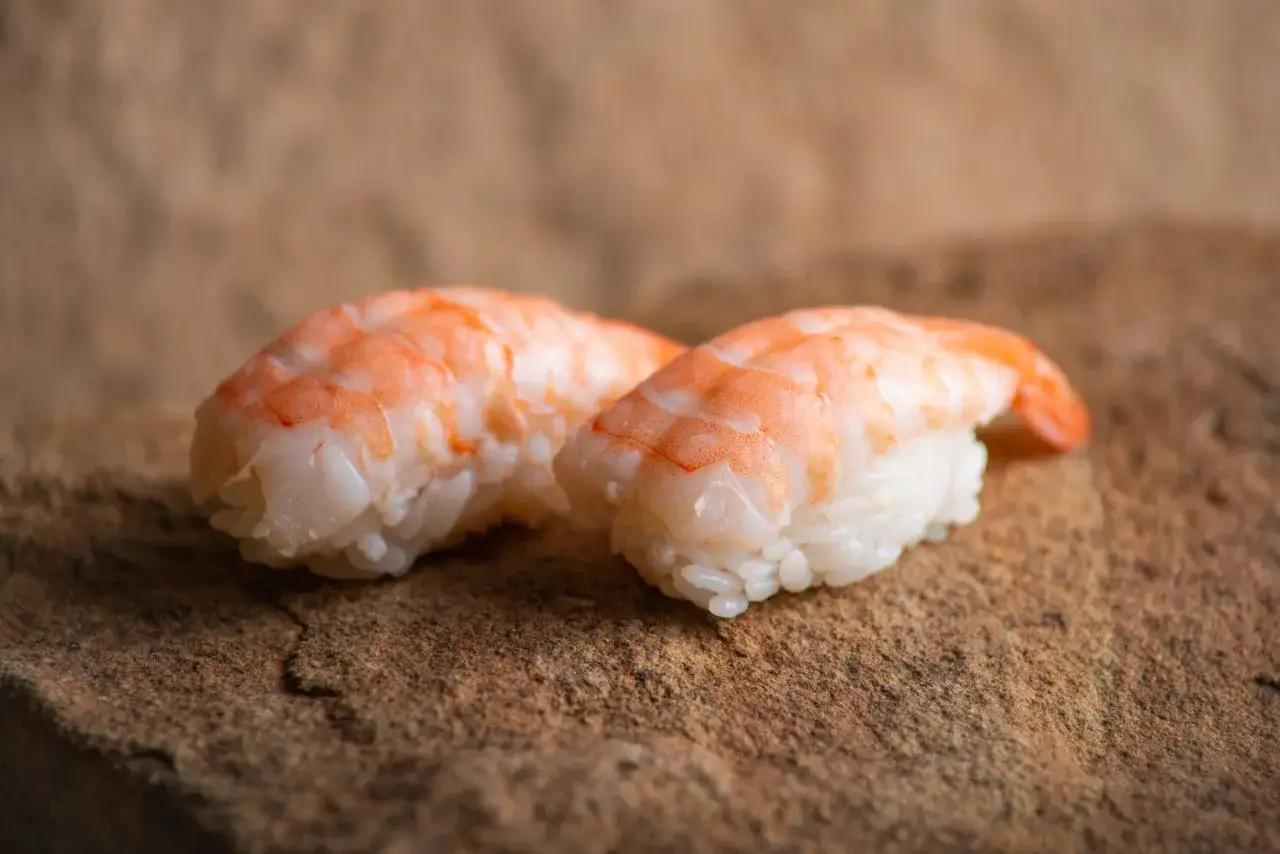 Dwa kawałki sushi z krewetkami, ułożone na kamiennej powierzchni. Idealne krewetki do sushi.