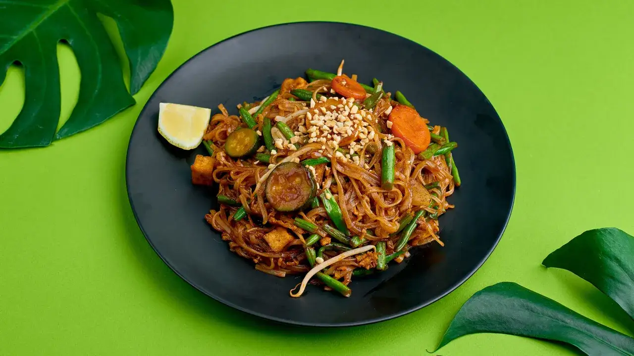 Pyszne pad thai z wołowiną, makaronem ryżowym, warzywami i orzeszkami ziemnymi na czarnym talerzu.