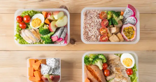 Cztery pojemniki z kolorowymi, zdrowymi posiłkami typu bentos: kurczak, ryż, warzywa i owoce.