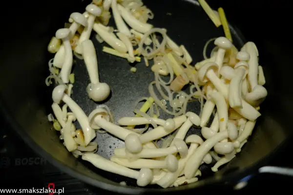Grzybki shimeji smażą się na patelni z cebulką i imbirem, tworząc aromatyczne danie.