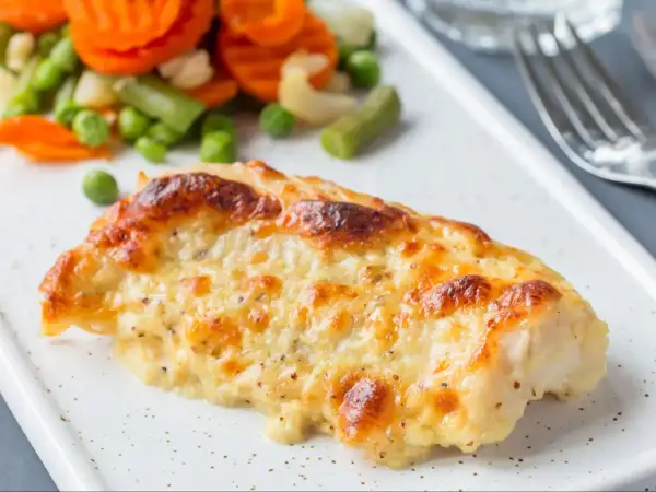 Pyszny, zapieczony filet z dorsza w sosie serowym, podany z kolorowymi warzywami.