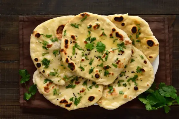 Stos chlebków naan, posypanych kolendrą i czarnuszką, z widocznymi pęcherzykami powietrza. Idealne do curry, ale warto sprawdzić chlebek naan kcal.