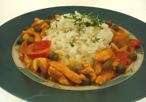 Pyszne tajskie curry z kurczakiem, podane z ryżem i zielonym groszkiem. Danie ozdobione jest świeżymi ziołami.