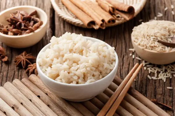 Miseczka parującego congee, obok miseczki z ryżem, anyżem i laskami cynamonu.