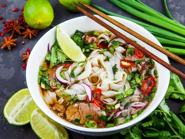 Aromaticzny makaron pho z wołowiną, świeżą kolendrą, cebulą i chili. Podany z limonką i pałeczkami.