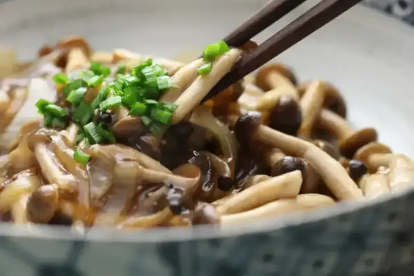Chopsticks podnoszą pyszne, duszony chińskie grzyby, posypane zieloną cebulką.