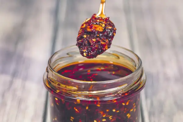 Łyżeczka z aromatycznym chili w oleju nad słoikiem pełnym tej pikantnej przyprawy.