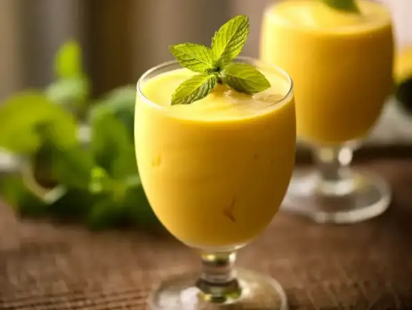 Gęsty, kremowy mango lassi w kieliszku, ozdobiony listkami mięty. Idealny na orzeźwienie.