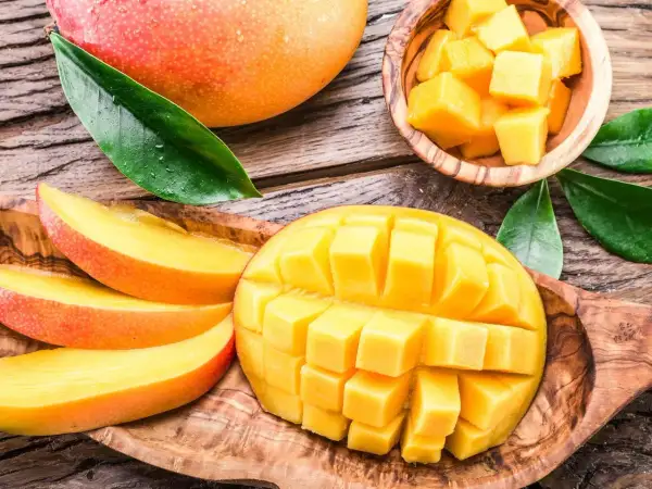 Soczyste, pokrojone w kostkę i plastry mango, które pokazuje, co to jest mango. Całe, dojrzałe owoce i liście na drewnianym tle.