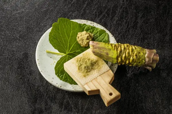 Świeżo starty chrzan japoński na tradycyjnej tarce. Obok liść i kawałek korzenia wasabi.