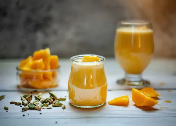 Słodki jogurt z mango, udekorowany kawałkami owoców, obok miseczki z mango i kardamonu.