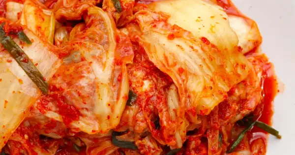 Pikantna kapusta kimchi, z widocznymi liśćmi i przyprawami, gotowa do podania.