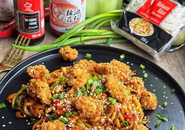 Pyszny udon z kurczakiem i warzywami, posypany sezamem i szczypiorkiem. Obok sos sojowy i opakowanie makaronu udon.