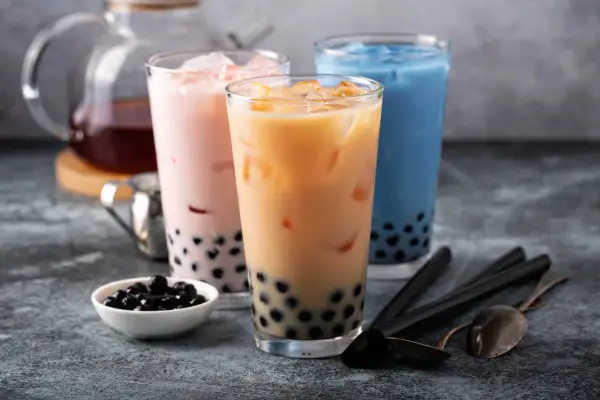 Trzy kolorowe napoje z tapioką, czyli co to jest bubble tea. Różowy, beżowy i niebieski napój z lodem i czarnymi kuleczkami.