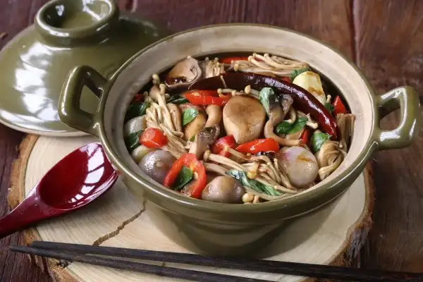 Aromatyczne danie z grzybkami mun, papryczką chili i innymi warzywami w glinianym garnku.