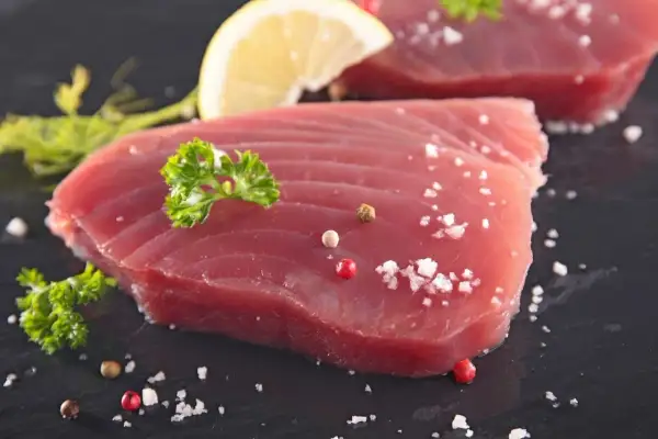 Świeży tuńczyk filet, doprawiony solą i pieprzem, z plasterkiem cytryny i natką pietruszki. Gotowy do grillowania.