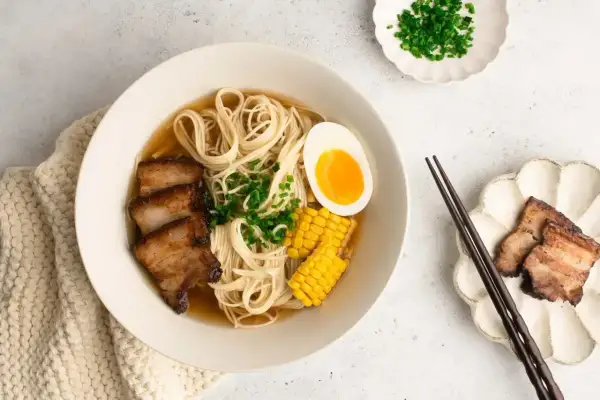 A miseczce shoyu ramen z makaronem, plastrami boczku, jajkiem na pół, kukurydzą i szczypiorkiem.