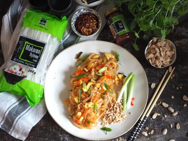 Pyszny pad thai z wołowiną, makaronem ryżowym i orzeszkami ziemnymi. Obok składniki: makaron, sos i płatki chili.