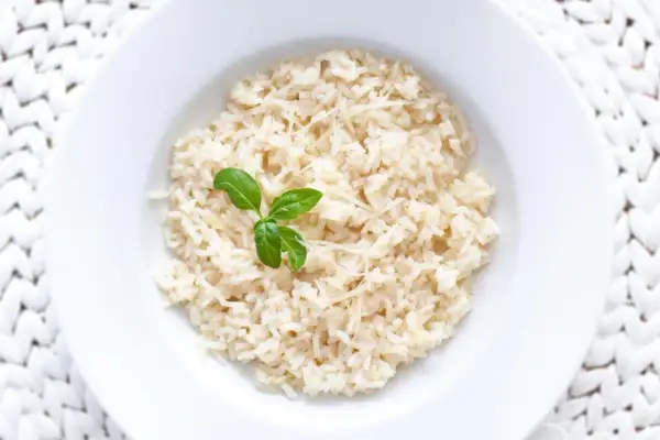 Ryż parboiled co to? Gotowany ryż z parmezanem i listkiem bazylii na białym talerzu.