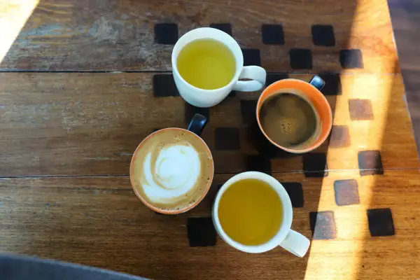 Kawa i herbata na drewnianym stole. Czy zielona herbata pobudza? Obok kawy latte i czarnej, dwie filiżanki z zieloną herbatą.