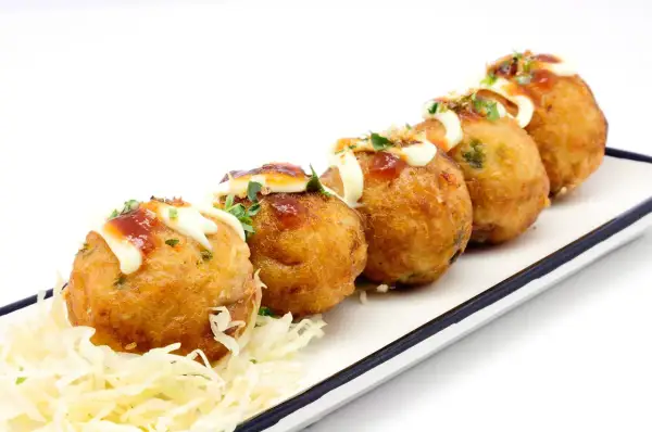 Pięć złotych kulek takoyaki, polanych majonezem i sosem, na białym talerzu z poszatkowaną kapustą. Idealne japońskie przekąski, przepisy na nie są proste!