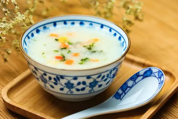 Misternie zdobiona miseczka z congee, czyli tradycyjną azjatycką owsianką z warzywami. Obok leży łyżka.