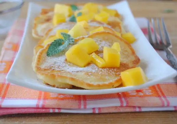 Puszyste placuszki z cukrem pudrem i kostkami mango, ozdobione listkami mięty. Idealne śniadanie z mango.