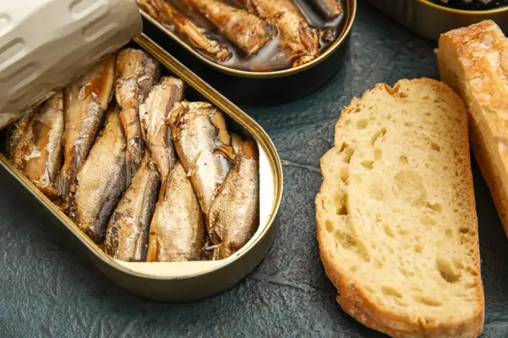 Otwarta puszka ryb wędzonych, obok kromki chleba. Czy ryby wędzone a cholesterol to temat do dyskusji?